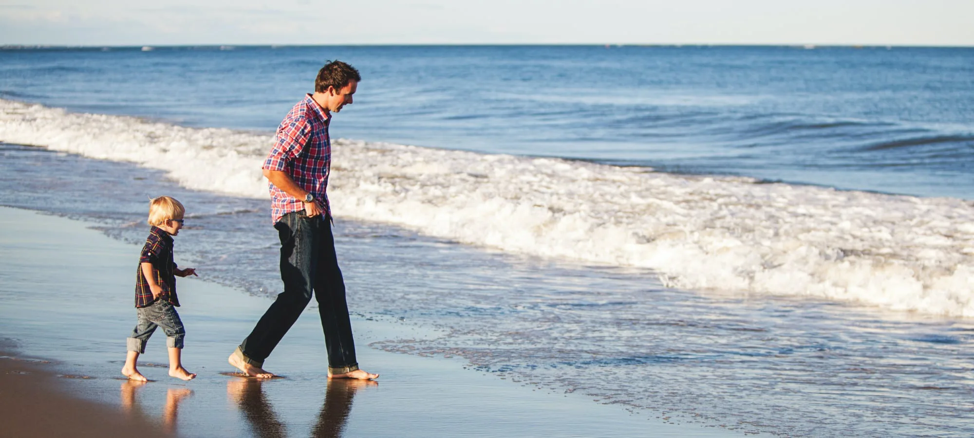 man and young boy walking on the beach towards the water