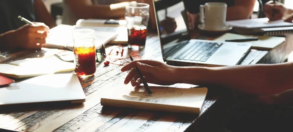 close up of a wooden desk with drinks, notepads and laptops