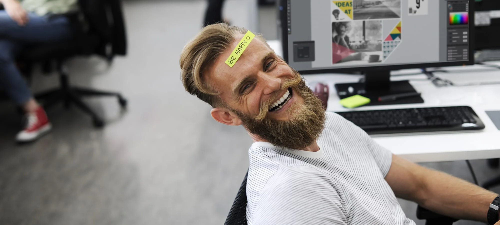 office worker sitting in chair and smiling with a post it note on his forehead
