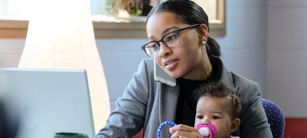 Mother holding baby and working at her computer