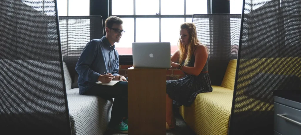 two colleagues in an office pod looking at a laptop screen