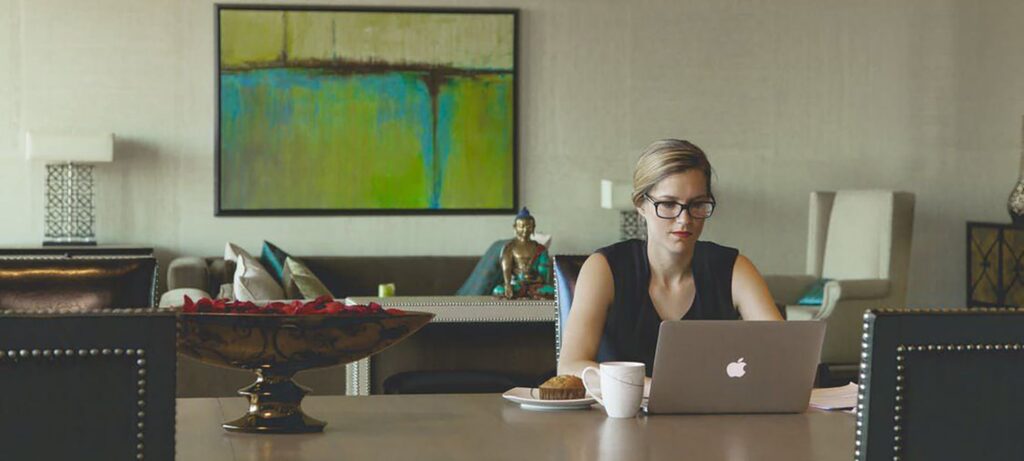 woman working at her laptop on a table with a big piece of artwork behind her