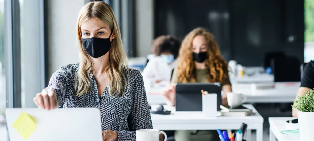 woman wearing a mask at a desk with a laptop open