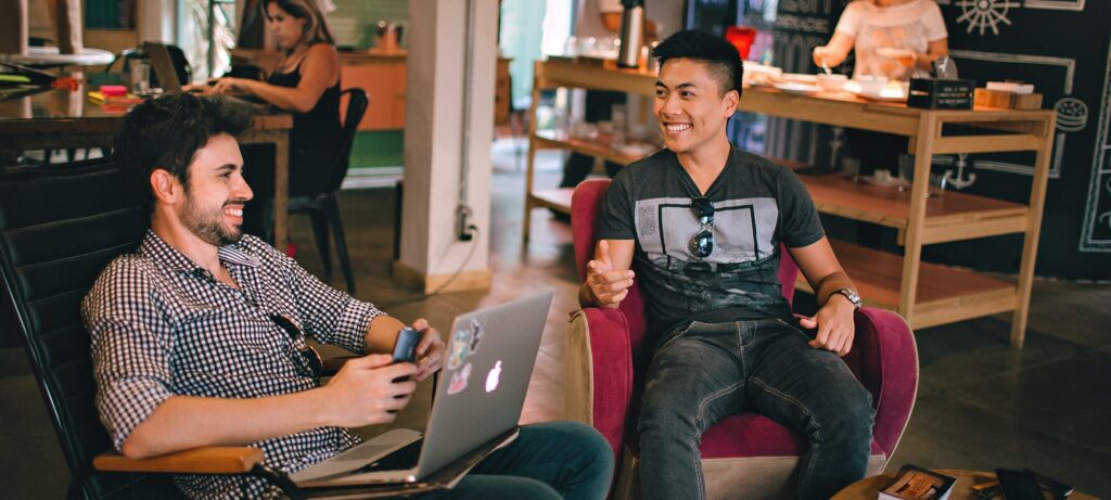 two male colleagues sat in armchairs with laptops