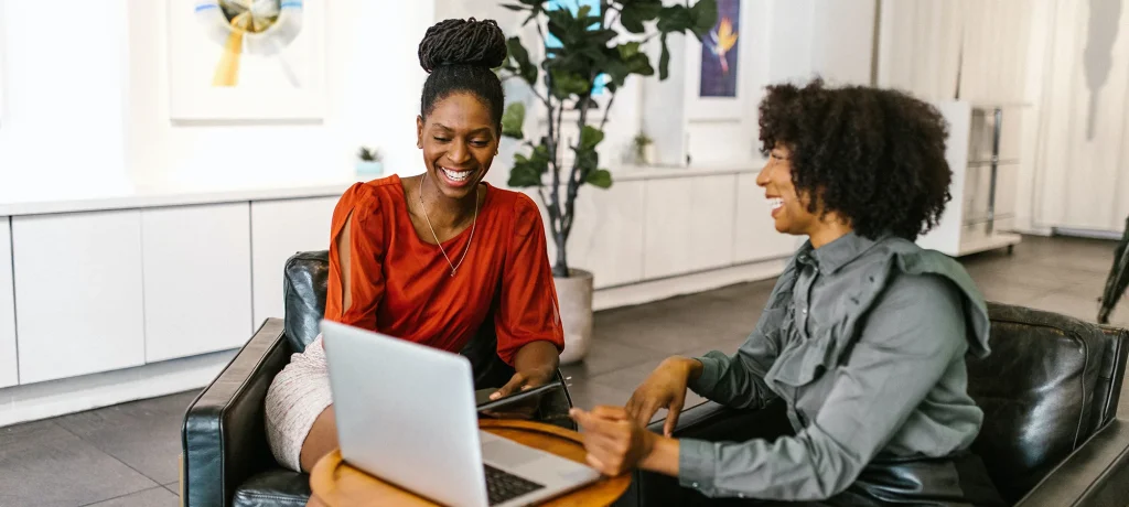 two female office workers laughing together as they look at a laptop screen